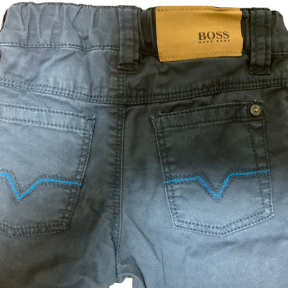 Close-up of the back waistband and pockets of dark gray denim jeans, showing a tan BOSS leather patch, a metal button, and bright blue zigzag contrast stitching.